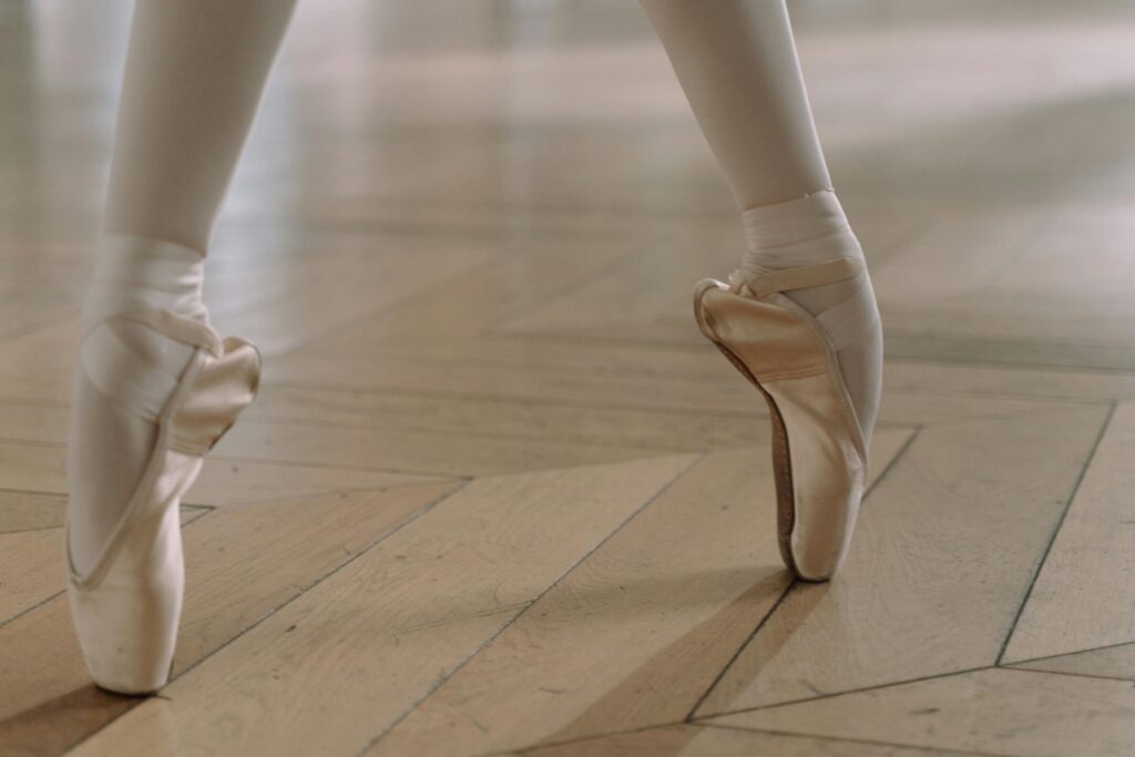 Close-up of a ballerina's feet in pointe shoes, showcasing grace and balance on a wooden floor.